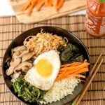 This amazing Korean Cauliflower Bibimbap recipe is delicious, low-carb, keto friendly, and easy to make. The perfect quick vegetarian weeknight dinner idea. Black bowl, bobimbap, sriracha